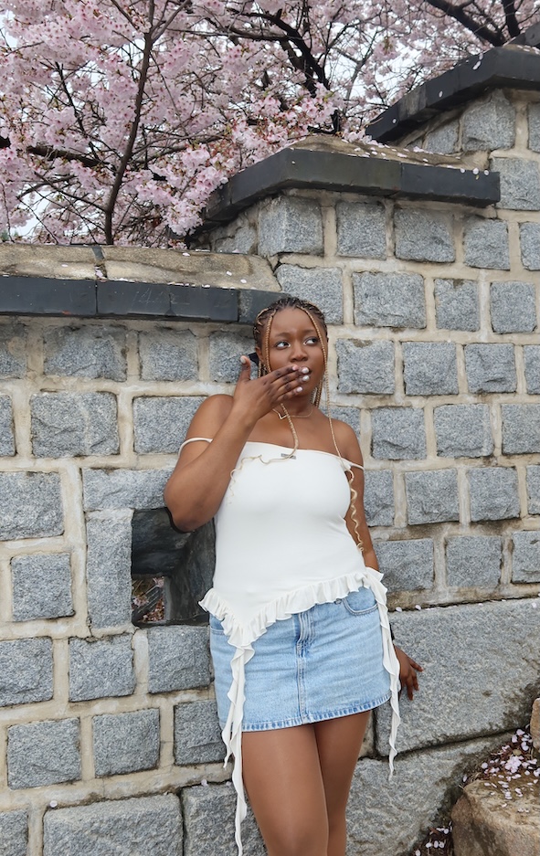 Marthal '27 standing by a wall with flowering Cherry trees behind it