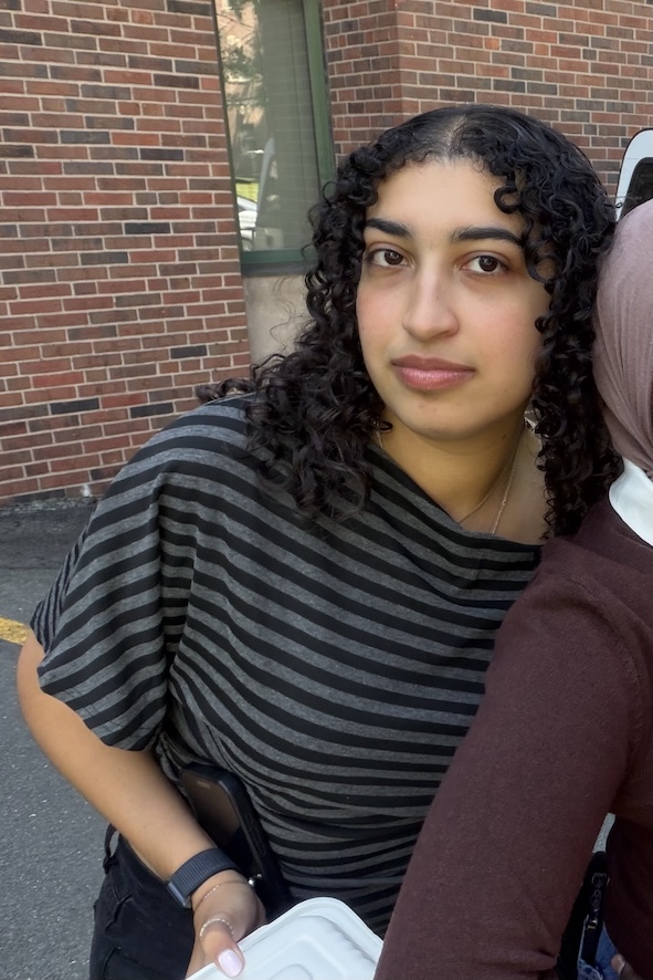 Leila posing by a brick wall in a striped shirt